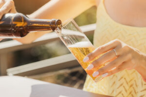 Mädchen schenkt aus einer Flasche in ein Glas ein und trinkt ein köstliches traditionelles deutsches und kölsches Bier in einem Biergarten oder Café im Freien