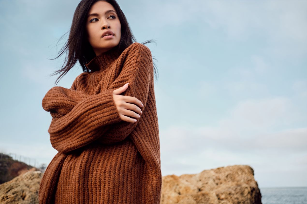 Frau am Strand im oversized braunen Strickpullover – idealer Look für alle, die pullover kaufen möchten