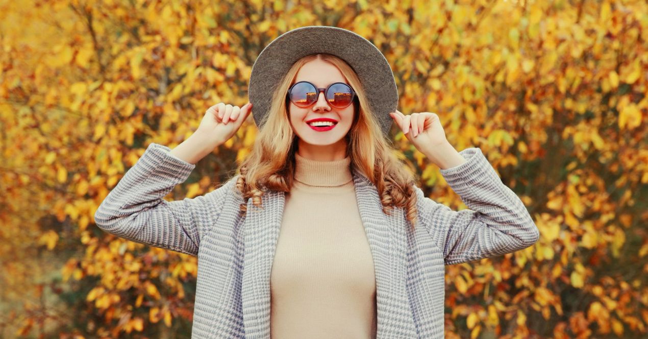 Frau mit Hut, Sonnenbrille und beigem Rollkragenpullover vor Herbstlaub – perfekter Style zum pullover kaufen