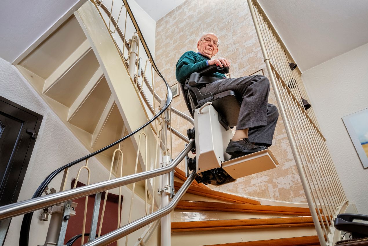 Aelterer Mann nutzt Treppe Lift auf einer gewundenen Treppe fuer mehr Unabhaengigkeit im Alltag