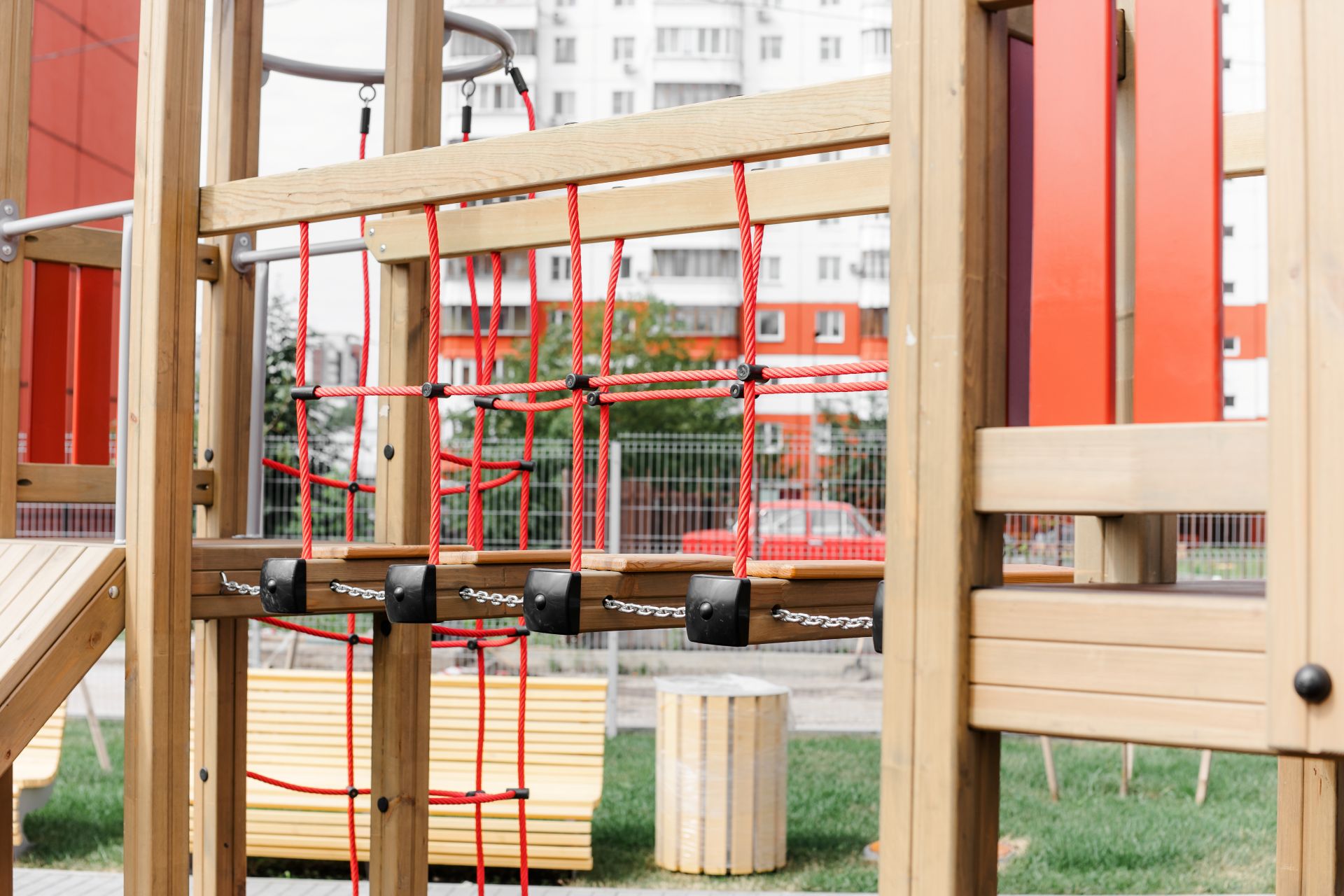 Detailaufnahme eines stabilen Holz-Klettergerüsts mit roten Seilen und Ketten auf einem modernen Spielplatz in der Stadt